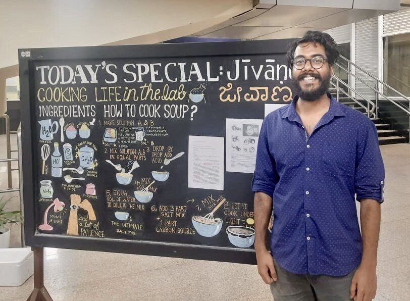 Nayan Chakraborty, the lead author of the present study in front of the exhibit’s display board at Indiranagar Metro Station; Picture Credits: Nishant N, Art Credits: Kriti Aggarwal.
